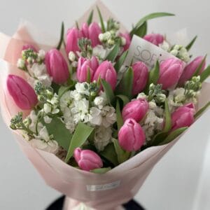 Vibrant bouquet featuring pink tulips and white flowers wrapped in soft pink paper, displayed on a black stand at SOFIORI flower shop in Calgary.